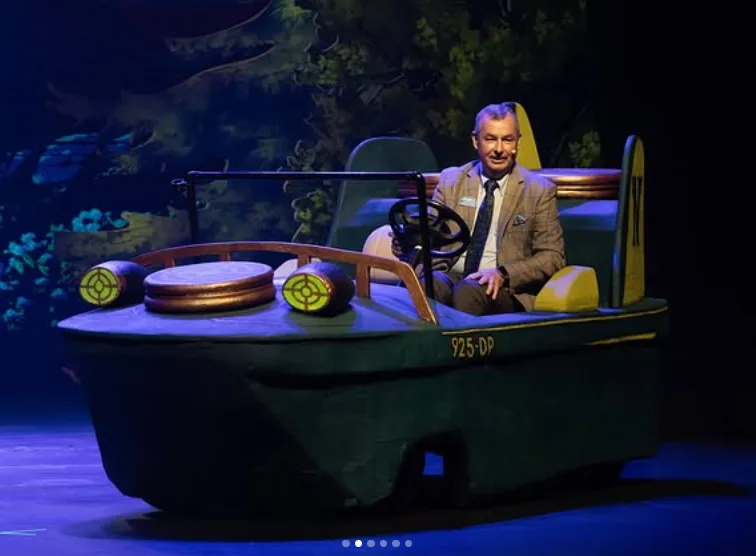 Dollywood President Eugene Naughton rode onto the stage in a themed prop vehicle during the NightFlight Expedition ceremony. Parton later joined the event by video after missing the celebration in person.