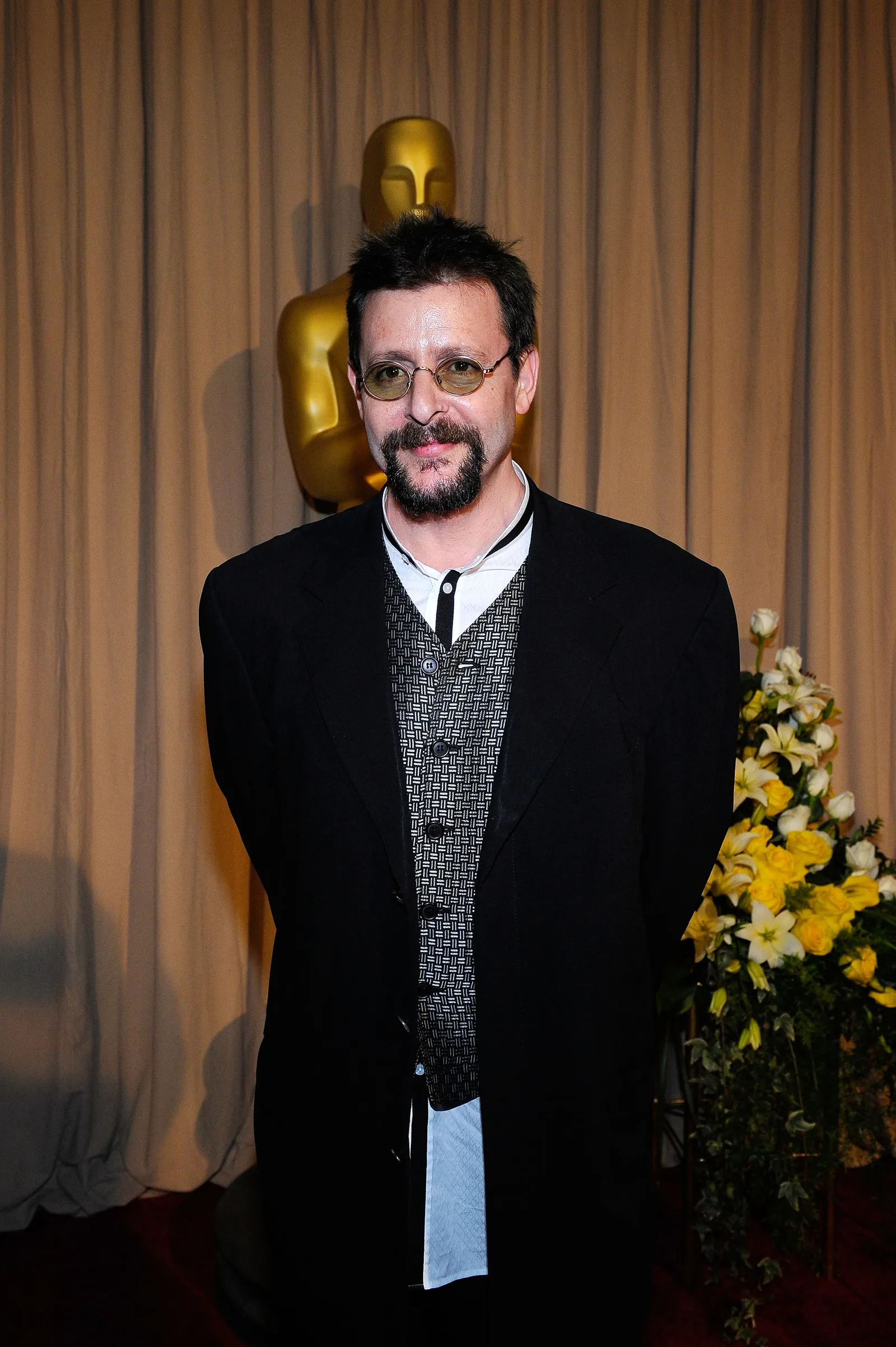 Posing backstage near a golden Oscar statuette at the 82nd Annual Academy Awards on March 7, 2010, the actor paired a patterned vest and dark coat with small tinted glasses and a neatly trimmed goatee.