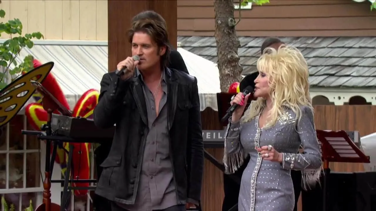 Performing live together: Dolly Parton, elegant in a grey sequined dress, and Billy Ray Cyrus sing duets on stage during an outdoor concert appearance.