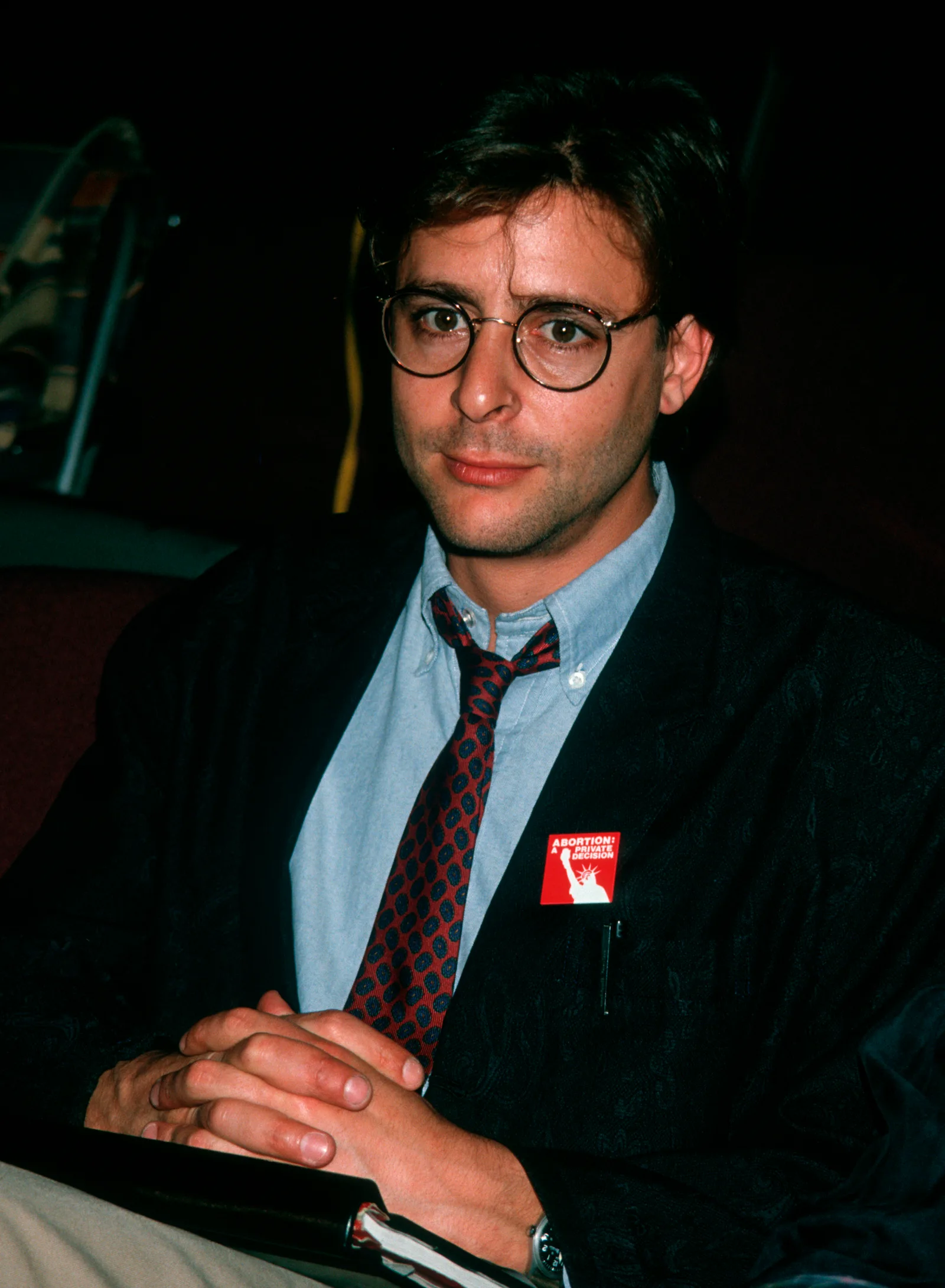 Seated with hands clasped during the first rehearsal for the stage play "Carnal Knowledge" at the Kaufman Theater in New York City, the actor paired round-framed glasses and a patterned tie with an advocacy pin on his blazer lapel.