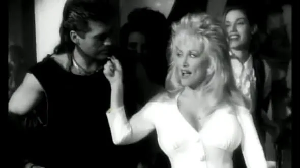 A classic 90s moment: Dolly Parton and Billy Ray Cyrus feature together in this black and white still, showcasing their iconic styles from the era.