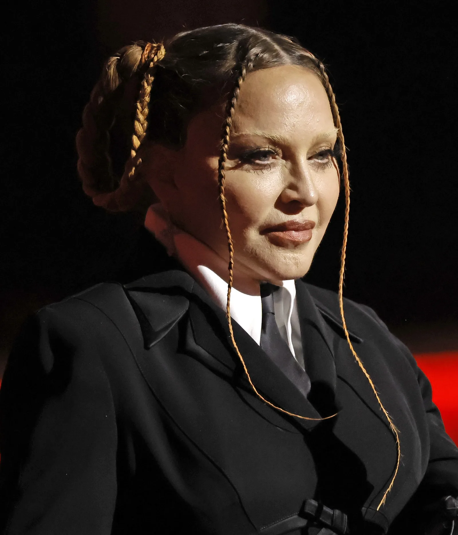Madonna is pictured in a sharply tailored black suit and tie, with her hair swept back and thin braids framing her face.