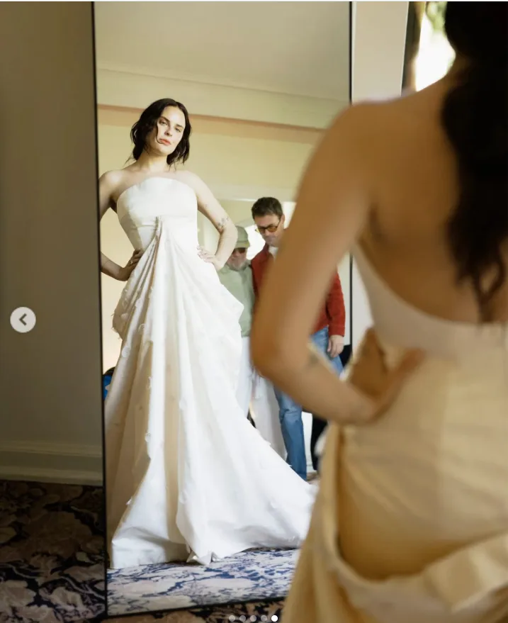 Tallulah Willis checks the fit of her custom Balenciaga gown in the mirror, offering a striking view of the strapless front and flowing train while the dress’s open back remains visible in the foreground.