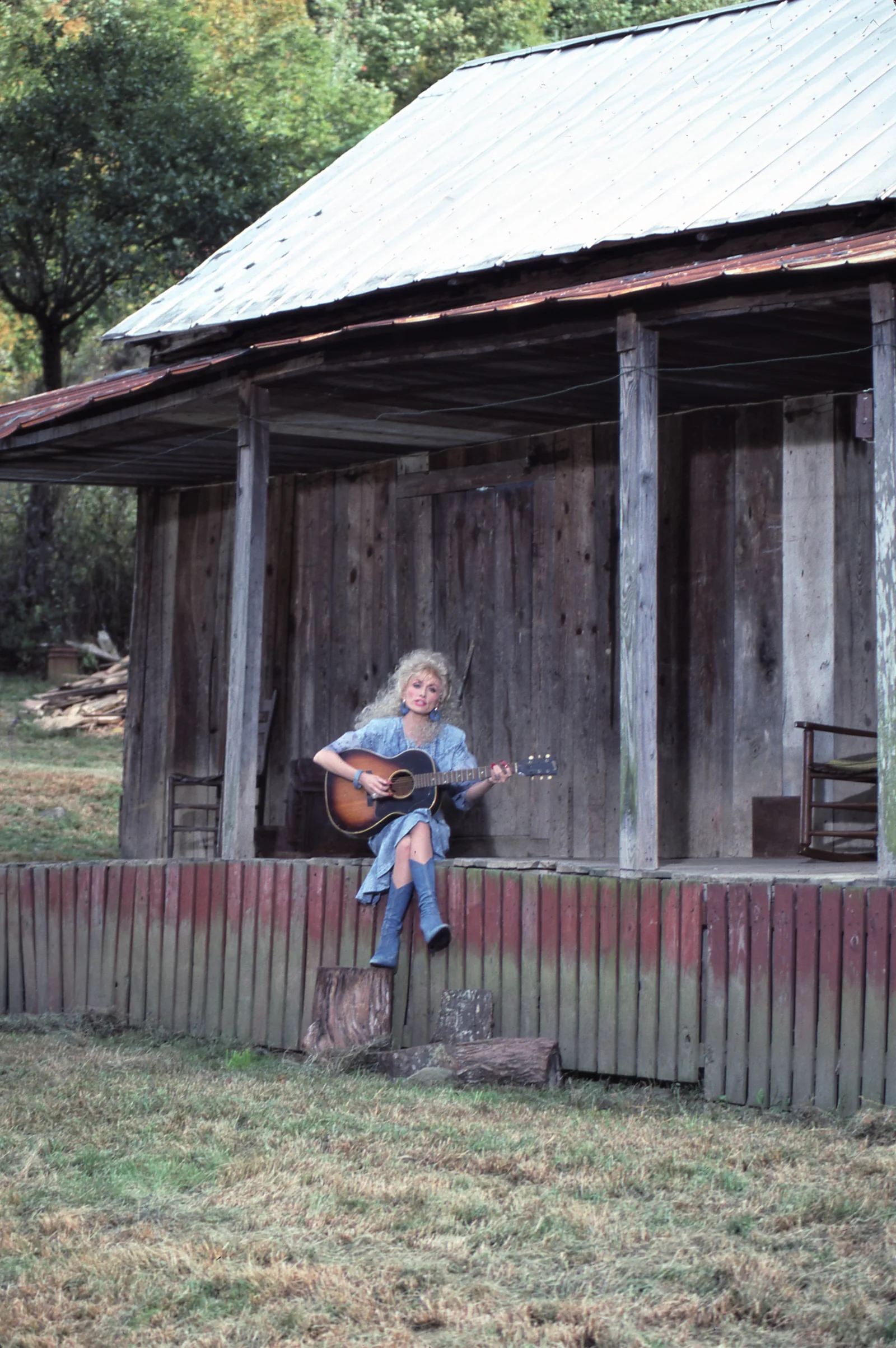 Decades after those childhood performances, Parton returned to the porch with the guitar that had become one of the defining symbols of her career — a striking contrast between the star she became and the humble setting where her musical ambitions began.