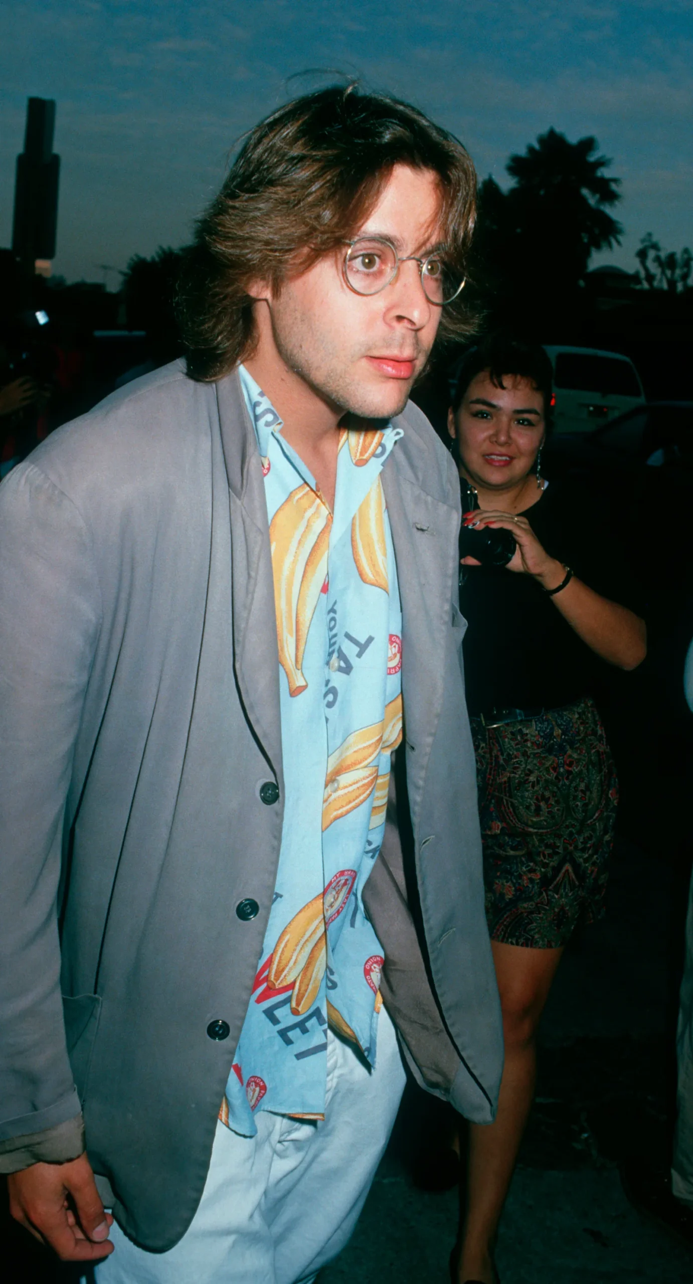 Showcasing a casual late-eighties look in a banana-print shirt, wire-rimmed glasses, and a grey blazer, the actor arrives at the UA Coronet Theater in Westwood for the premiere of "Young Guns."