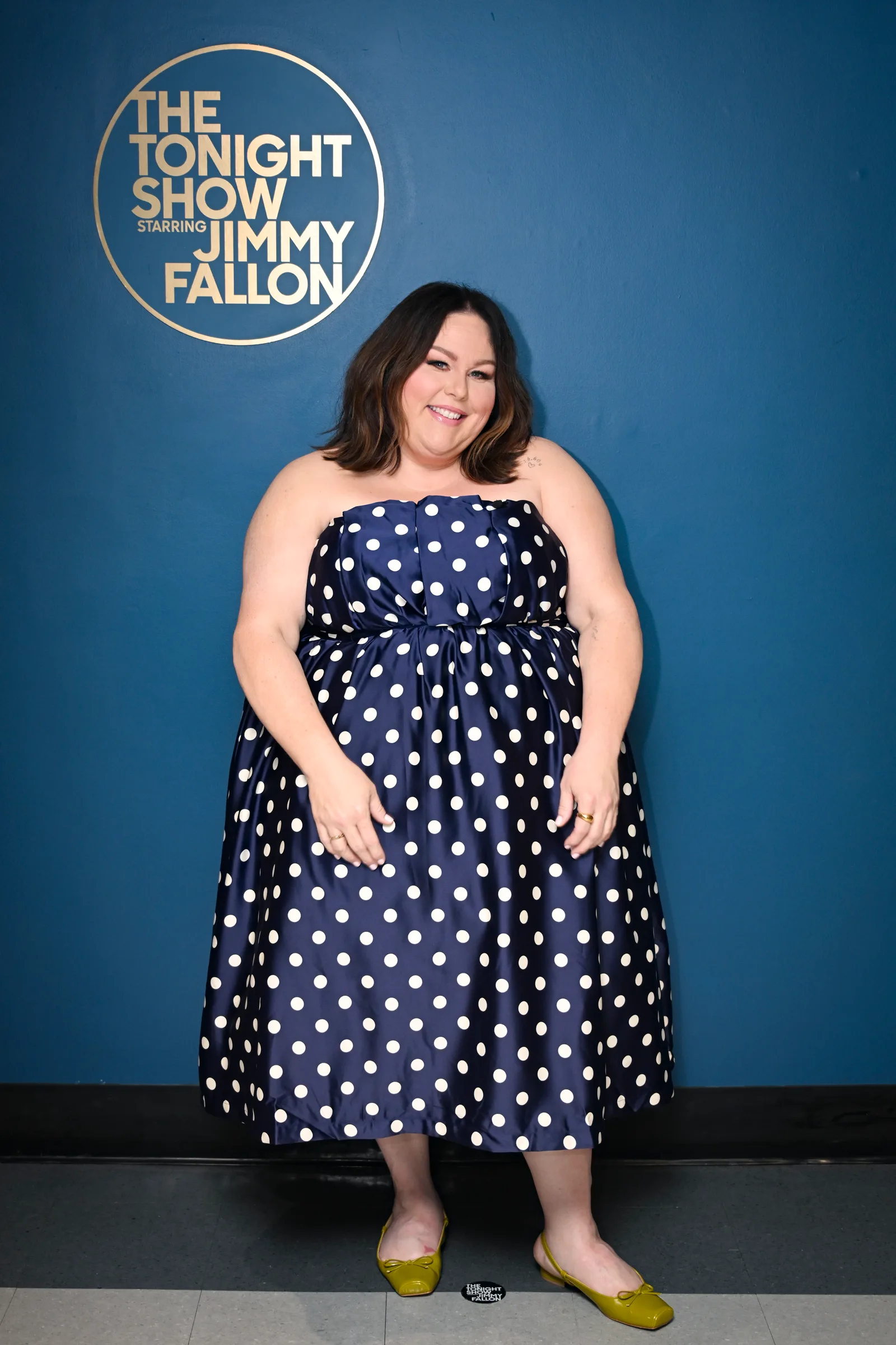 Metz posed backstage at "The Tonight Show Starring Jimmy Fallon" in a navy polka-dot midi dress with yellow flats. The photo shows a later stage of her transformation after she began using a GLP-1.