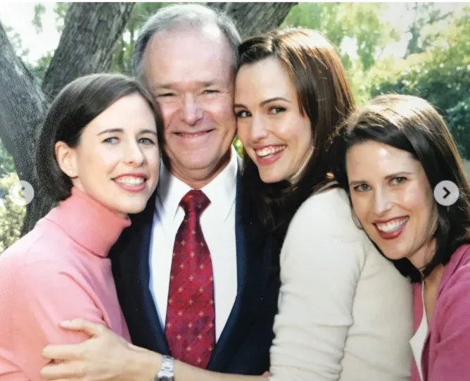 William Garner smiles as his daughters gather around him beneath a tree in a family portrait included in Jennifer Garner's Father's Day carousel. The image captures the close bond the actress and her sisters shared with their late father.