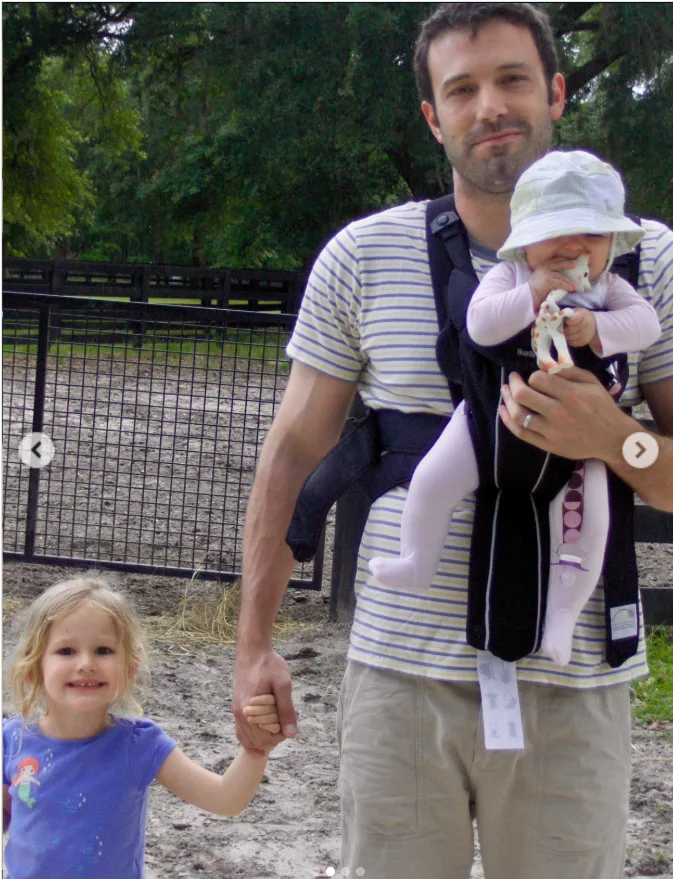 Ben Affleck walks hand in hand with one daughter while carrying another in a baby carrier during a visit to what appears to be an animal enclosure. The candid throwback photo was one of two images Jennifer Garner included in her Father's Day tribute that quietly honored the father of her three children.
